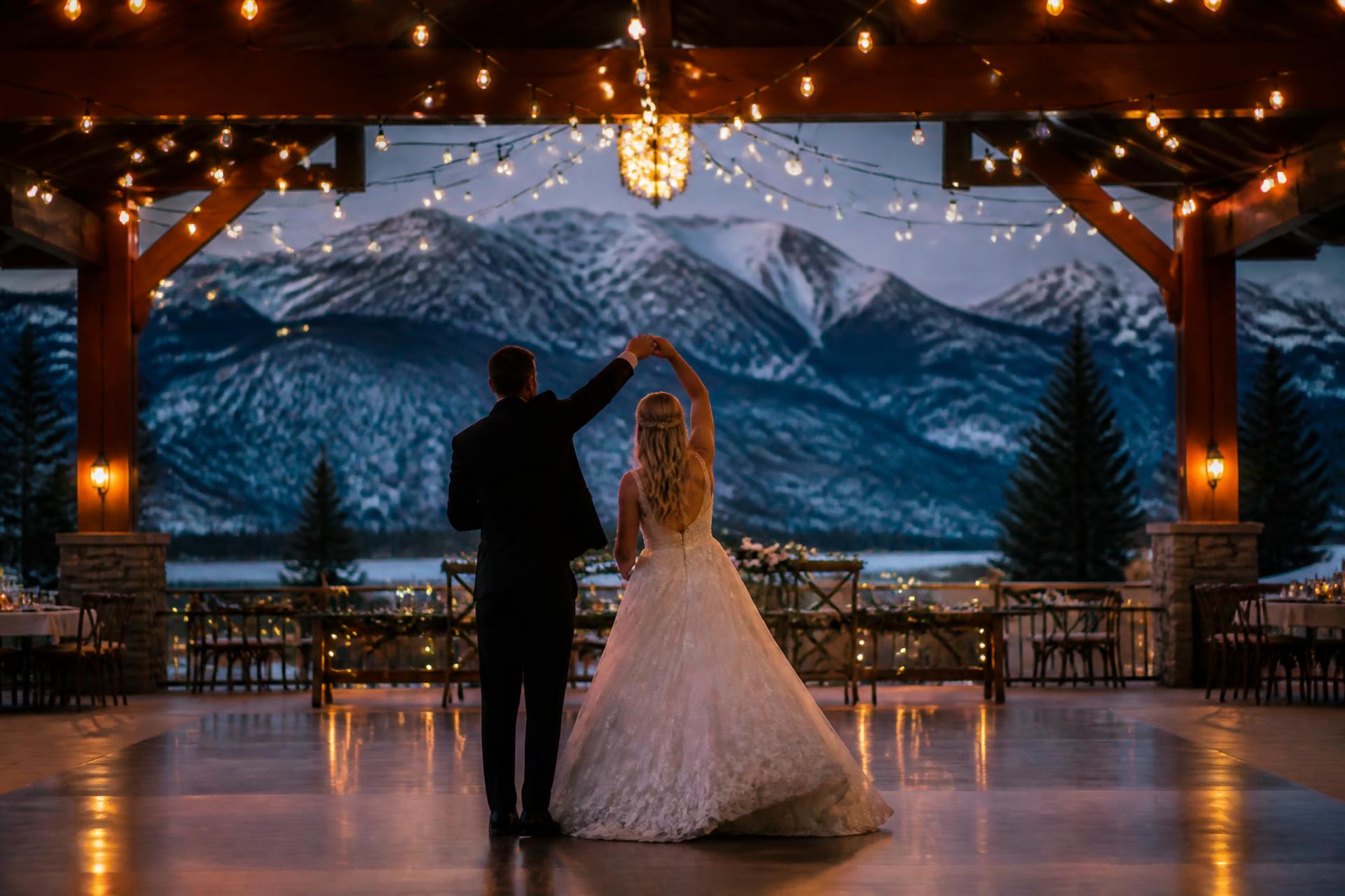 Couple's first dance under string lights with mountain backdrop